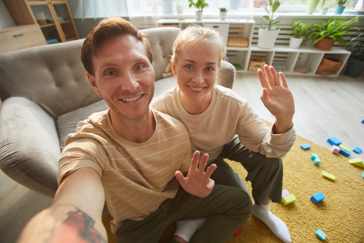 A couple at home greeting someone with a friendly wave during a video call.
