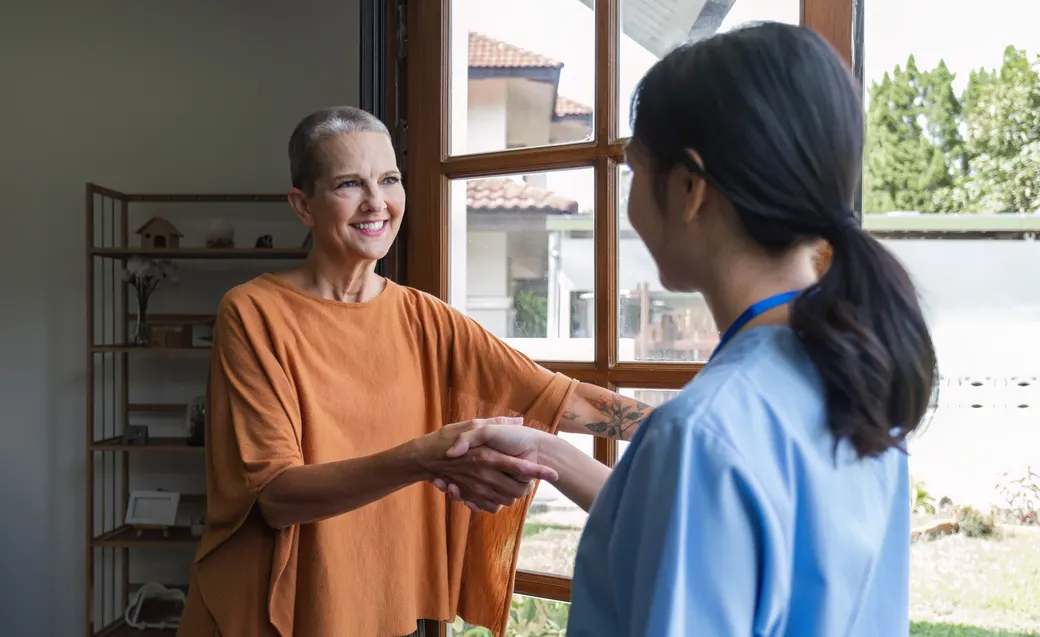 A healthcare professional warmly greeting a client with a handshake at a home visit.