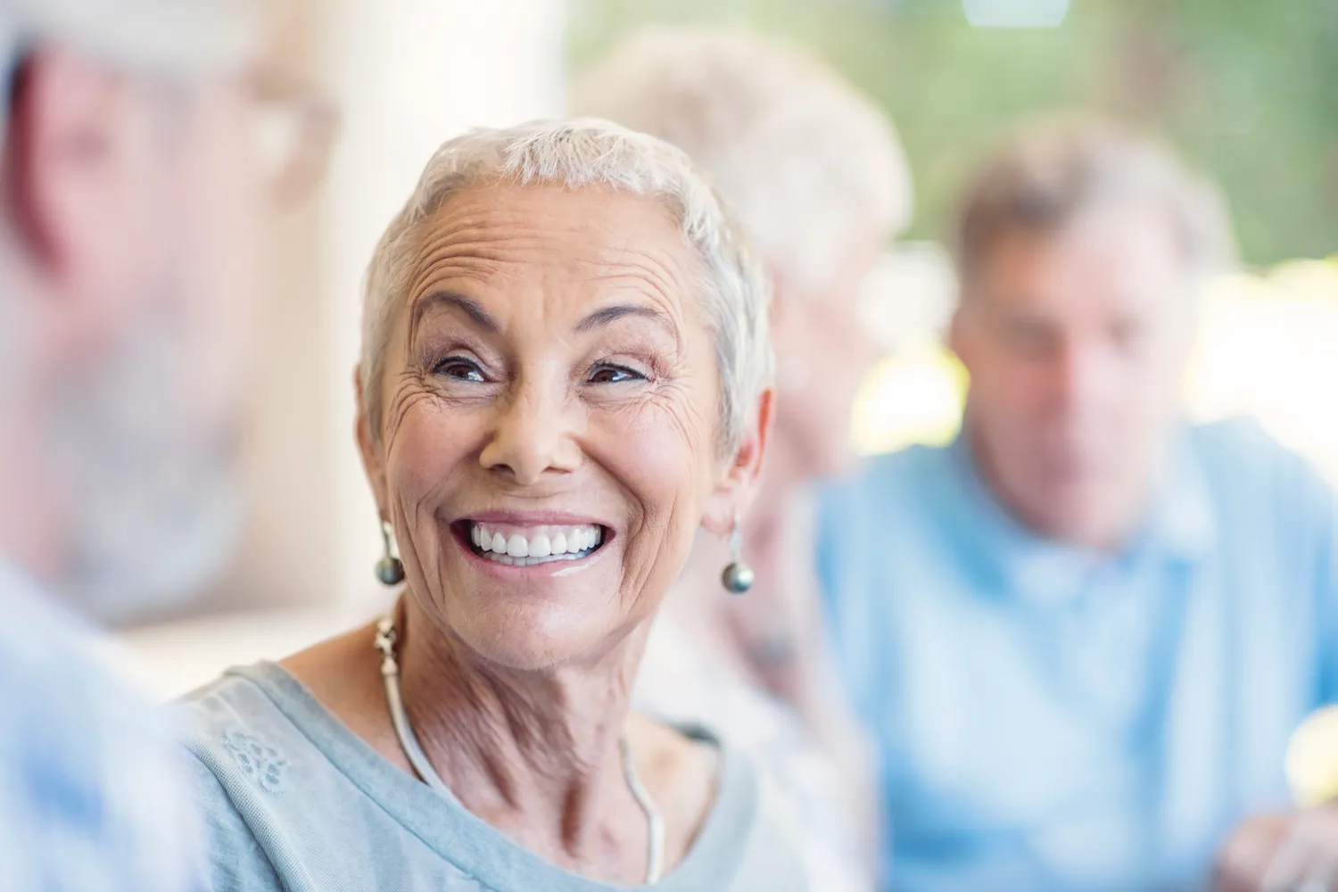 A smiling older woman with short silver hair laughing warmly with friends.