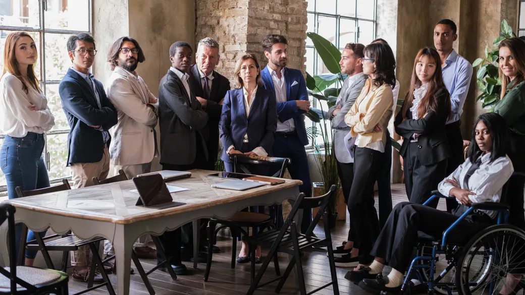 A diverse team standing together in a bright, modern office, including a wheelchair user.