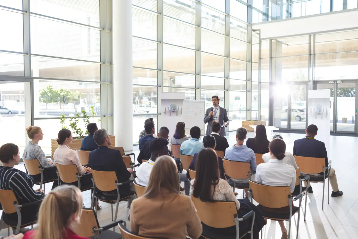 A speaker presenting to an engaged, seated audience in a bright modern training session.