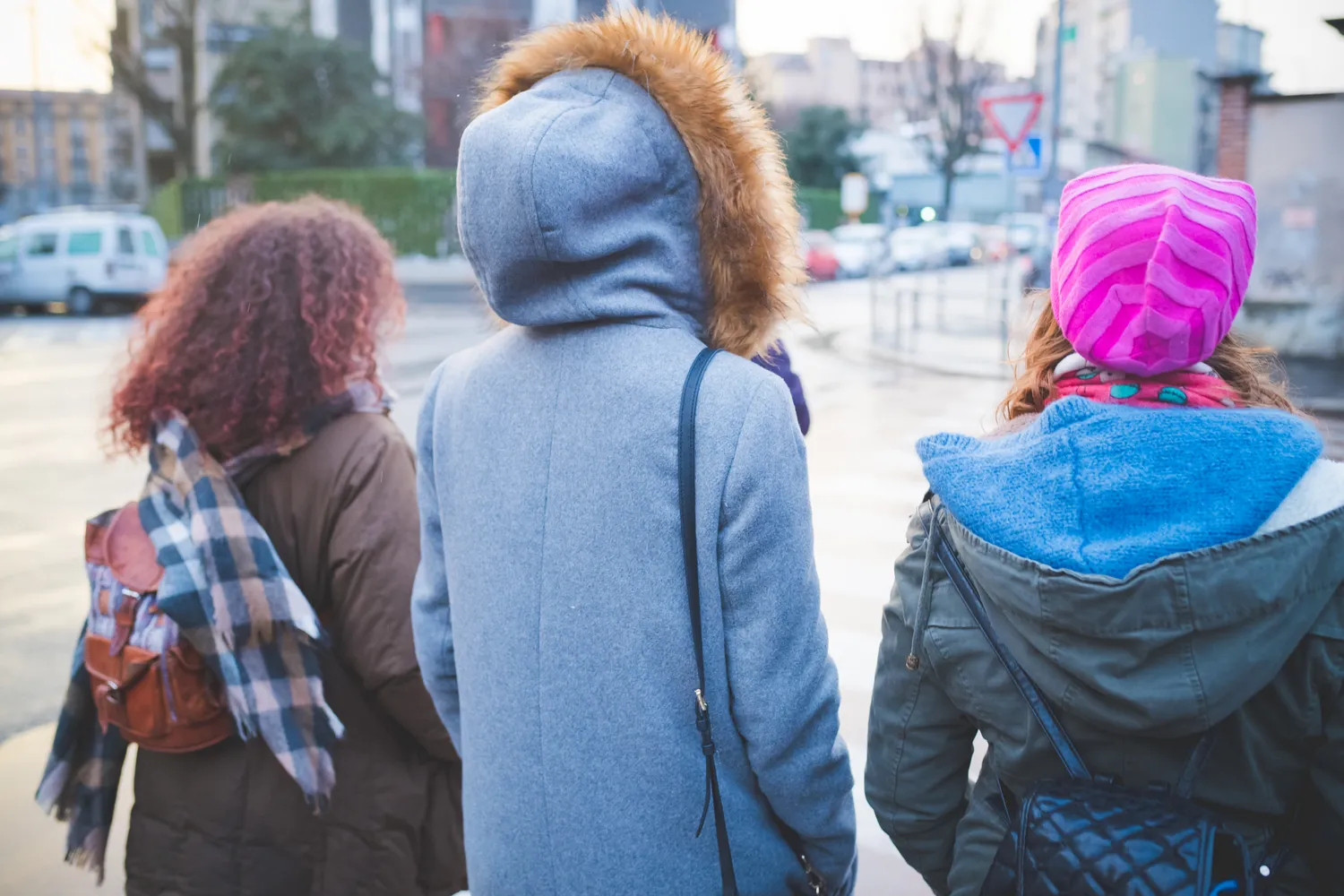 Three young women in winter coats walking together along a city street.